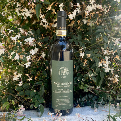 Montenidoli Vernaccia wine bottle standing among white flowers, green label with 2021